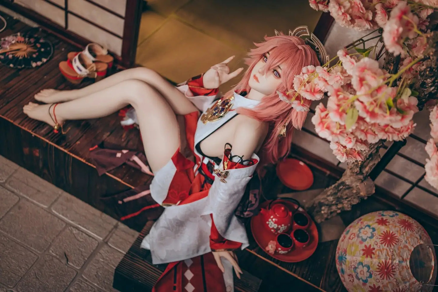 Yae Miko Genshin Impact cosplay sex doll, pink hair, sensual miko outfit, tatami room red cup – anime cosplay lifesize doll by TopLoveDoll, red bell anklet, wooden geta sandals, Genshin Impact sex doll, sitting on the stairs, legs crossed, holding a J-style red cup, high-angle full shot, horizontal profile, doing a rock'n'roll gesture