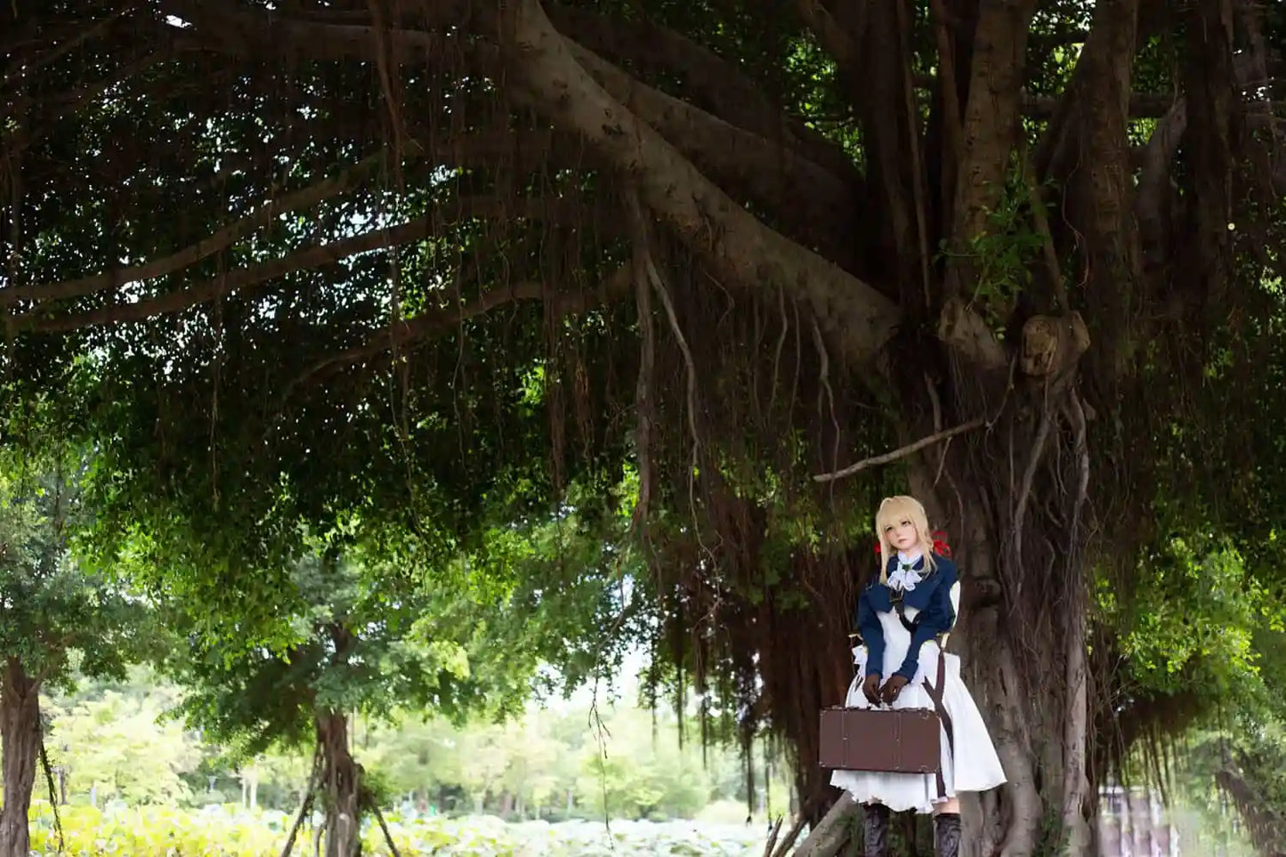Aliana, golden straight long hair, blue eyes, navy Auto Memory Doll uniform, white apron, black leather boots, outdoor, green trees, standing under a huge tree with a lot of vines and green leaves, brown gloves, holding a brown leather suitcase, eye-level shot,grand scene, front side view – Violet Evergarden cosplay anime sex doll by TopLoveDoll