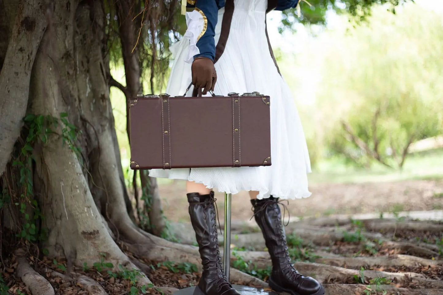 Aliana, golden straight long hair, blue eyes, navy Auto Memory Doll uniform, white apron, black leather boots, outdoor, standing under a huge tree with a lot of vines and green leaves, brown gloves, holding a brown leather suitcase, suitcase close up, side view, doing the salute gesture, horizontal profile – Violet Evergarden cosplay anime sex doll by TopLoveDoll