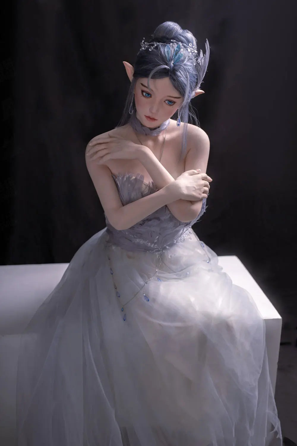 Alisha silver-blue hair, porcelain skin, pointed ears, floral tulle and feather gown, fantasy pose, three-quarter shot, sitting and holding her arms, front view, looking down– lavender elf fantasy sex doll by TopLoveDoll
