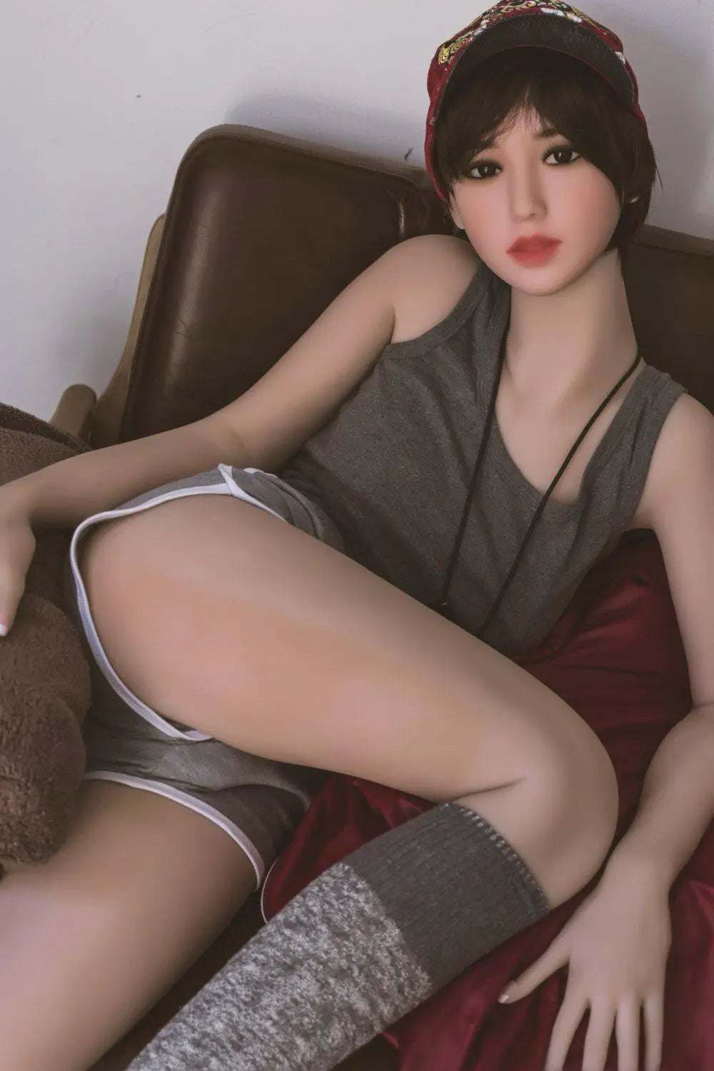 Amira short dark brown hair red lip grey tank denim shorts red jacket tomboy feminine contrast pose, sitting in the sofa chair sexily – girl-next-door companion sex doll by TopLoveDoll