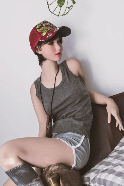 Amira short dark brown hair red lip grey tank denim shorts red jacket tomboy feminine contrast pose, sitting on the arm of the chair, baseball hat, red sunglasses on the neck lace,– girl-next-door companion sex doll by TopLoveDoll