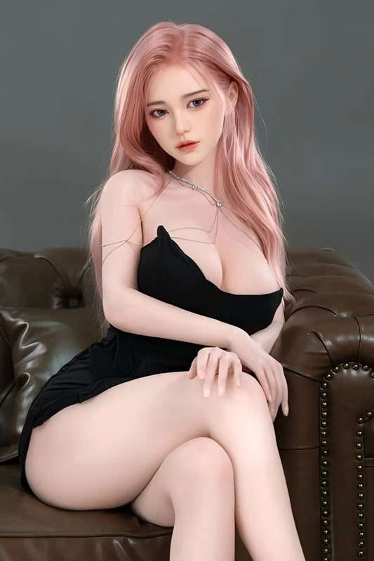 Blackpink Sora sex doll – busty asian pink hair K-pop idol sex robot doll with long straight rose-pink hair in black deep-V strapless mini dress and silver body chain, full body seated on leather sofa front view with legs crossed, lifelike love doll by TopLoveDoll